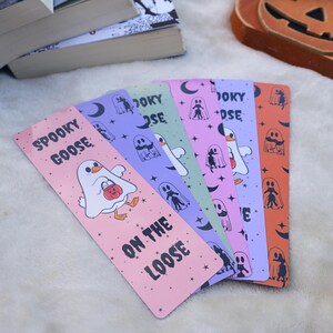 A set of several halloween-themed bookmarks. Alternating between bookmarks with geese dressed as ghost with the quote "spooky goose on the loose" and bookmarks with ghosts holding black cats  with moons and stars.