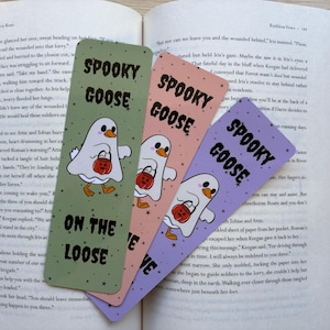 a set of three bookmarks with a goose in the center dressed as a ghost with a candy bucket, and the words read "spooky goose on the loose" Colors are green, orange, and purple with tiny black stars.