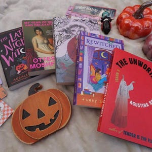 Several halloween themed bookmarks paired with several books. Glass pumpkins in the background