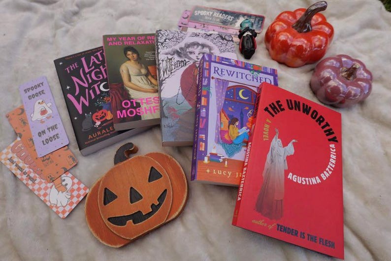 Several halloween themed bookmarks paired with several books. Glass pumpkins in the background