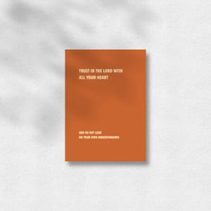 Könnte beinhalten: Ein rechteckiger Druck mit einem einfarbigen, gebrannten orangefarbenen Hintergrund und weißem Text, der lautet: TRUST IN THE LORD WITH ALL YOUR HEART AND DO NOT LEAN ON YOUR OWN UNDERSTANDING. Das Design ist in einer klaren, vertikalen Ausrichtung.
