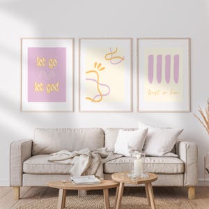 Könnte beinhalten: Drei gerahmte Kunstdrucke mit minimalistischen Designs. Die Drucke zeigen Pastellfarben und inspirierende Texte: "let go let god" und "trust in him". Das Kunstwerk wird über einem beigen Sofa mit hölzernen Beistelltischen ausgestellt.