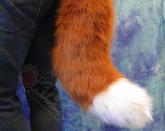 May include: A fluffy orange and white fox tail costume accessory. The tail is attached to a person's waist with a belt loop.