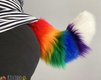 May include: A plush, faux fur tail featuring a vibrant rainbow gradient pattern that transitions from red, orange, yellow, and green to blue, purple, and a solid white tip. The tail is attached to a dark garment and displays a soft, thick texture.
