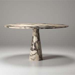 May include: A round marble table with a single, conical base. The tabletop and base feature a mix of beige, grey, and black veining. The table is approximately 76 cm in diameter.