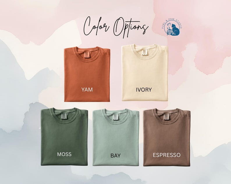 May include: Five folded t-shirts in various colors: yam, ivory, moss, bay, and espresso. The text "Color Options" is written in cursive at the top, with a logo in the upper right corner. The background has a watercolor effect.