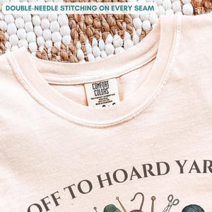 May include: Cream-colored t-shirt with the text "OFF TO HOARD YARN" and various yarn-related graphics. The shirt features double-needle stitching on the seams and a Comfort Colors label.