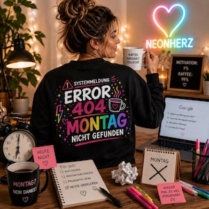 Könnte beinhalten: Ein schwarzes Langarm-Sweatshirt mit einer bunten Grafik auf der Rückseite mit dem Text SYSTEMMELDUNG ERROR 404 MONTAG NICHT GEFUNDEN, einem Blitz, einem Herz und einem Kaffeetassen-Symbol, getragen von einer Person mit einer weißen Tasse.