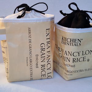 May include: Two beige fabric bags with black drawstrings. One bag has a white interior and a tag. The other bag has a black interior. Text on the bags reads "Extra Fancy Long Grain Rice" and "Kitchen Essentials".
