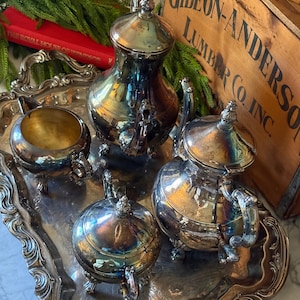 May include: A silver-plated tea service set consisting of a tall teapot, a shorter teapot, a lidded sugar bowl, and an open creamer, all featuring ornate feet and handles, arranged on a matching rectangular silver-plated serving tray with decorative edges.