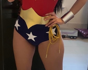May include: A woman wearing a red and blue Wonder Woman costume with a gold belt and a gold rope. She is wearing silver bracelets and red boots with white stripes.