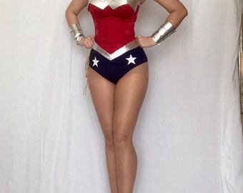 May include: A red and blue Wonder Woman costume with a silver star and a silver design on the bodice. The costume is worn by a person with long dark hair and white heels.