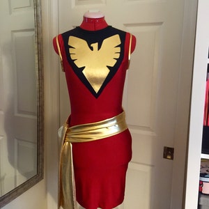 Könnte beinhalten: Ein rotes, ärmelloses Kleid mit einem schwarzen und goldenen Phönix-Design auf dem Oberteil. Das Kleid hat einen goldenen Gürtel aus Metall.