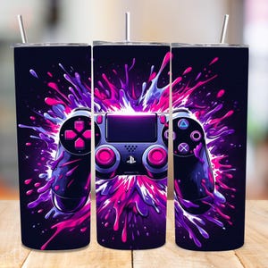 Könnte beinhalten: Drei Edelstahlbecher mit einem Design einer Videospielkonsole. Die Konsole ist in Lila- und Rosatönen gehalten und vor einem dunklen Hintergrund mit einem Spritzeffekt dargestellt. Jeder Becher ist mit einem Strohhalm ausgestattet.