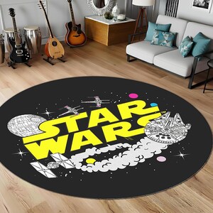 Puede incluir: Una alfombra redonda negra con las palabras "STAR WARS" en amarillo. El diseño incluye ilustraciones de la Estrella de la Muerte, el Halcón Milenario y cazas X-wing. La alfombra está colocada sobre un suelo de madera, de unos 150 cm de diámetro.