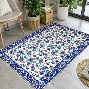 May include: Rectangular area rug with a white background and a floral pattern in blue, red, and teal. The rug has a detailed border in a darker blue. The design features stylized flowers and leaves.