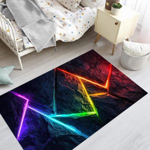 May include: A rectangular rug featuring a dark, textured design with bright neon geometric lines in red, orange, yellow, green, and blue. The rug is placed on a light-coloured wooden floor.