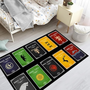 May include: Black rectangular area rug featuring the sigils of various houses from a fantasy series. Each house emblem is displayed on a colored background, including a stag, bear, and wolf. The rug is placed on a wooden floor.