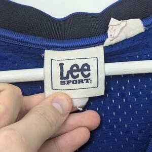 May include: Close-up of a blue mesh jersey with a navy blue collar. The jersey features a "Lee Sport" tag. The tag is white with black text. The jersey is hanging on a white hanger.