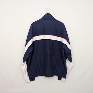 May include: Navy blue track jacket with white and red accents. The jacket features a full zipper, a high collar, and white stripes across the chest and sleeves. The cuffs and hem are finished with a red trim.