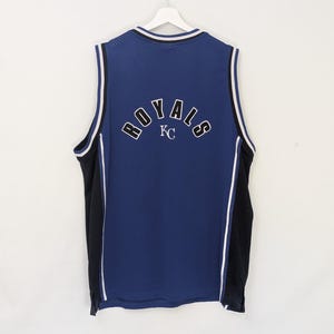 May include: A blue mesh jersey with the word "ROYALS" arched across the back in white lettering. The jersey has black side panels and white trim. The letters "KC" are below the word "ROYALS".
