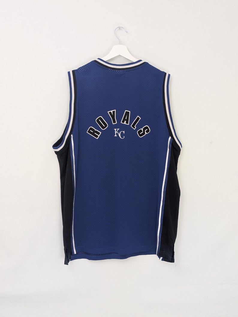 May include: A blue mesh jersey with the word "ROYALS" arched across the back in white lettering. The jersey has black side panels and white trim. The letters "KC" are below the word "ROYALS".