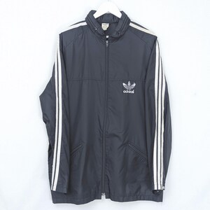 Op de afbeelding: Zwart Adidas trainingsjack met witte strepen op de mouwen en schouders. De jas heeft een volledige ritssluiting, een opstaande kraag en het Adidas-logo op de borst. Het hangt aan een witte hanger.