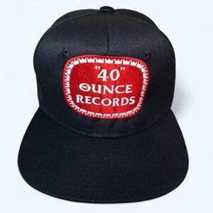 May include: Black baseball cap with a flat brim. The cap features a red patch with white trim, displaying the text "40 OUNCE RECORDS" in white lettering. The cap is a classic style, suitable for casual wear.