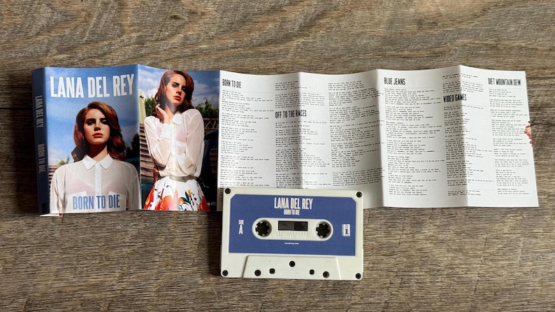 May include: A cassette tape and album art for Lana Del Rey's "Born to Die" album. The cassette is blue and white, with the album title printed on it. The album art features a photo of Lana Del Rey.