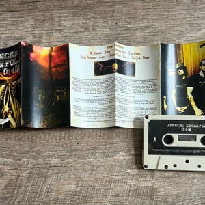 May include: A cassette tape and its accompanying booklet are displayed on a wooden surface. The cassette is labeled "Avenged Sevenfold City of Evil." The booklet features band photos and lyrics.
