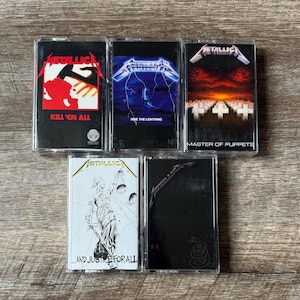 May include: Five vintage Metallica cassette tapes. The album covers feature bold graphics and text, including "Kill 'Em All," "Ride the Lightning," "Master of Puppets," "...And Justice for All," and the self-titled album.