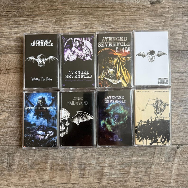 May include: A collection of eight cassette tapes featuring album art from the band Avenged Sevenfold. The tapes showcase various album covers with skulls, angels, and other gothic imagery. The album titles are visible on the cassette labels.