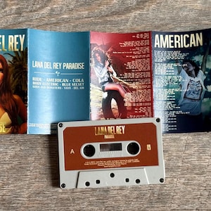 May include: A cassette tape and album art for Lana Del Rey's "Paradise" album. The cassette is brown and gray. The album art features the album title and a portrait of Lana Del Rey.
