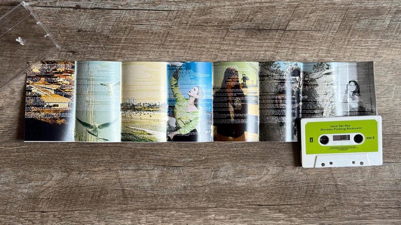May include: A cassette tape with a lime green label and white casing sits next to a folded booklet. The booklet features various images and text, including photos of people and landscapes. The cassette label reads "Lana Del Rey, Norman Fucking Rockwell".