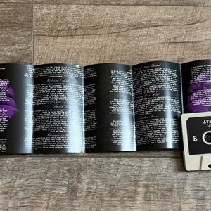 May include: A cassette tape and its insert are displayed. The cassette is off-white with black text and a black label. The insert is black with white text and purple floral accents. The cassette reads "Avenged Sevenfold" and "Waking the Fallen" on the label.