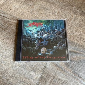 May include: A CD case with the album art for "Effigy of the Forgotten" by Suffocation. The artwork shows a battle scene with mechanical figures and a dark colour palette. The band's name is at the top, and the album title is at the bottom.