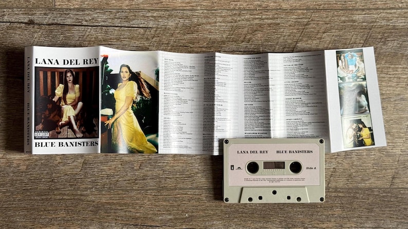 May include: A cassette tape and album booklet for Lana Del Rey's "Blue Banisters." The booklet features photos of the artist in a yellow dress. The cassette is light pink with the album title printed on it.