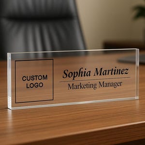 Peut inclure: Plaque de bureau en acrylique transparent avec le nom "Sophia Martinez" et le titre "Marketing Manager" en noir. Un carr&eacute; pour un logo personnalis&eacute; est &agrave; gauche. La plaque repose sur un bureau en bois.