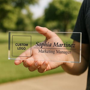 Peut inclure: Plaque de bureau en acrylique transparent avec le texte "Sophia Martinez, Marketing Manager". La plaque comporte &eacute;galement un espace pour un logo personnalis&eacute;. La plaque est rectangulaire et tenue dans une main.