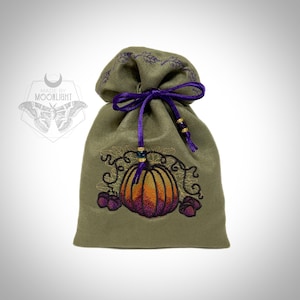 May include: An olive green drawstring pouch featuring an embroidered pumpkin with orange and purple gradient shading, surrounded by dark vines. The bag is cinched with a purple ribbon tied in a bow, accented with small beads, and includes a logo with the text MADE BY MOONLIGHT and a moth illustration.