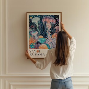 Puede incluir: Una impresi&oacute;n art&iacute;stica enmarcada con una ilustraci&oacute;n de acuarela de medusas en tonos azules, morados y naranjas. La impresi&oacute;n incluye el texto "YAYOI KUSAMA" en la parte inferior. La obra de arte se muestra contra una pared blanca.