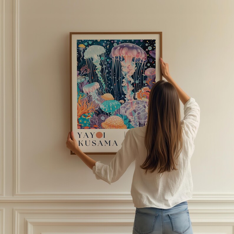 Puede incluir: Una impresi&oacute;n art&iacute;stica enmarcada con una ilustraci&oacute;n de acuarela de medusas en tonos azules, morados y naranjas. La impresi&oacute;n incluye el texto "YAYOI KUSAMA" en la parte inferior. La obra de arte se muestra contra una pared blanca.