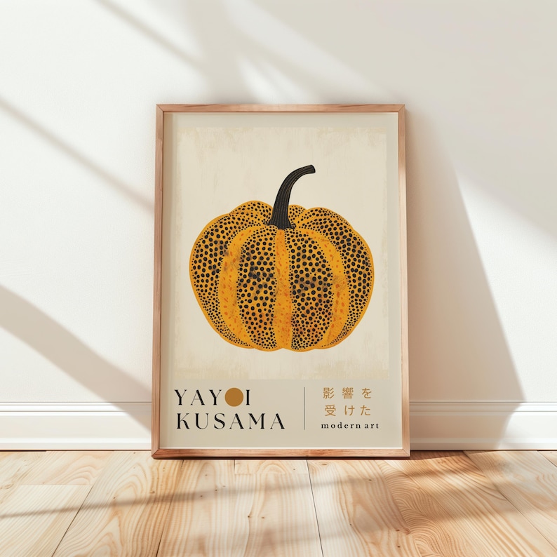 May include: A framed art print featuring a stylized pumpkin with a black stem and a yellow body covered in black dots. The print includes the name "YAYOI KUSAMA" and Japanese text, framed in a light brown wooden frame.