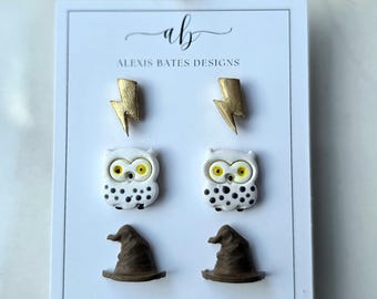May include: A white card displays six pairs of earrings. The top row features gold lightning bolt studs. Below are white owl studs with black spots and yellow eyes. The bottom row shows brown witch hat studs. The text "alexisbatesdesigns.etsy.com" is at the bottom.