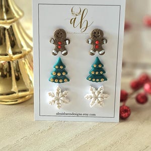 May include: A set of Christmas-themed earrings displayed on a white card. The earrings include gingerbread men, Christmas trees, and snowflakes. The card has the text "alexisbatesdesigns.etsy.com".