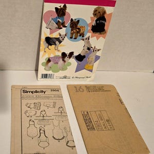 May include: A Simplicity 2904 sewing pattern envelope for dog clothing in sizes XS and S, featuring illustrations of dogs wearing various outfits, alongside two folded brown paper instruction sheets with diagrams and text for garment construction.