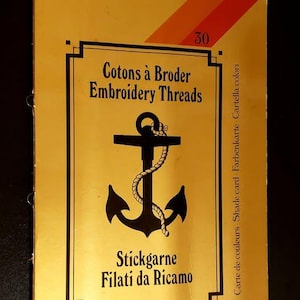 May include: A yellow box with black text and an anchor design. The text reads "Cotons à Broder Embroidery Threads" and "Stickgarne Filati da Ricamo". A number 30 is in the upper right corner. The box has a black border.