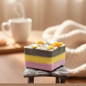 May include: A layered soy wax melt in pink, yellow, gray, and green, topped with yellow accents, sits on a small wooden stand. The text reads "Banana Split Bliss Soy Wax Melt" and "Experience Dessert-Inspired Fragrance!"