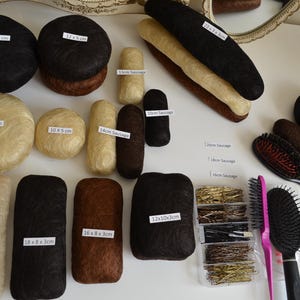 Puede incluir: Una variedad de accesorios para el cabello, que incluyen moños, piezas de cabello en forma de salchicha y cepillos para el cabello. Las piezas de cabello vienen en varios colores, incluyendo negro, marrón y rubio. Algunas piezas están etiquetadas con dimensiones, como 14 x 7 cm.