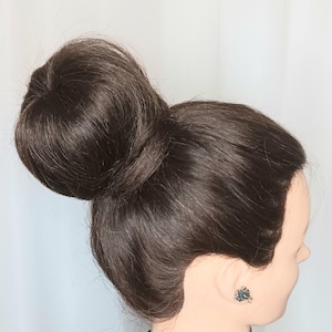 May include: A mannequin head with dark brown hair styled in a high bun. The hair is smooth and shiny. The mannequin is wearing a patterned top and a small, teal-coloured earring.